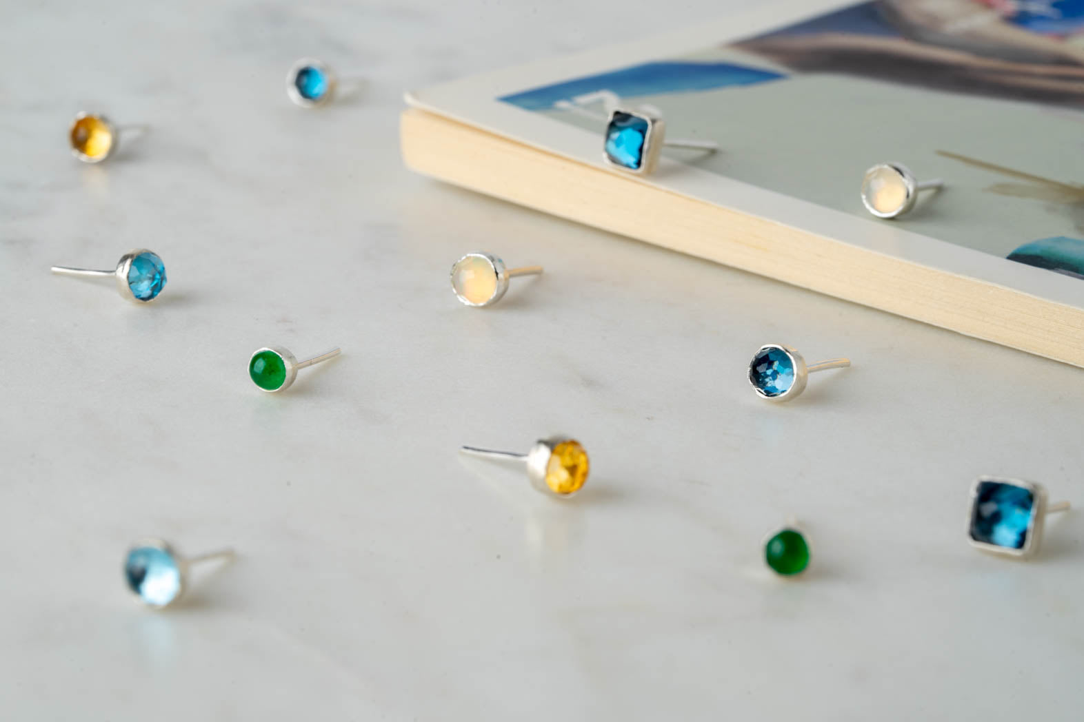 Handgjorda silverstuds med olika stenar på en marmorskiva – Nude Stockholm.