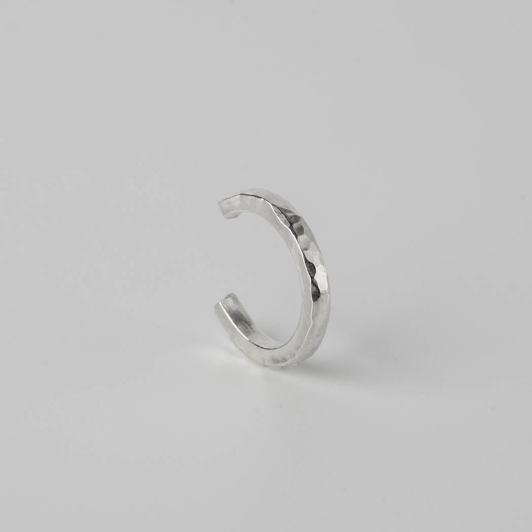 Ear cuff med hamrad design â handgjord i 925 sterlingsilver med en unik textur som reflekterar ljuset, fotograferad mot vit bakgrund.