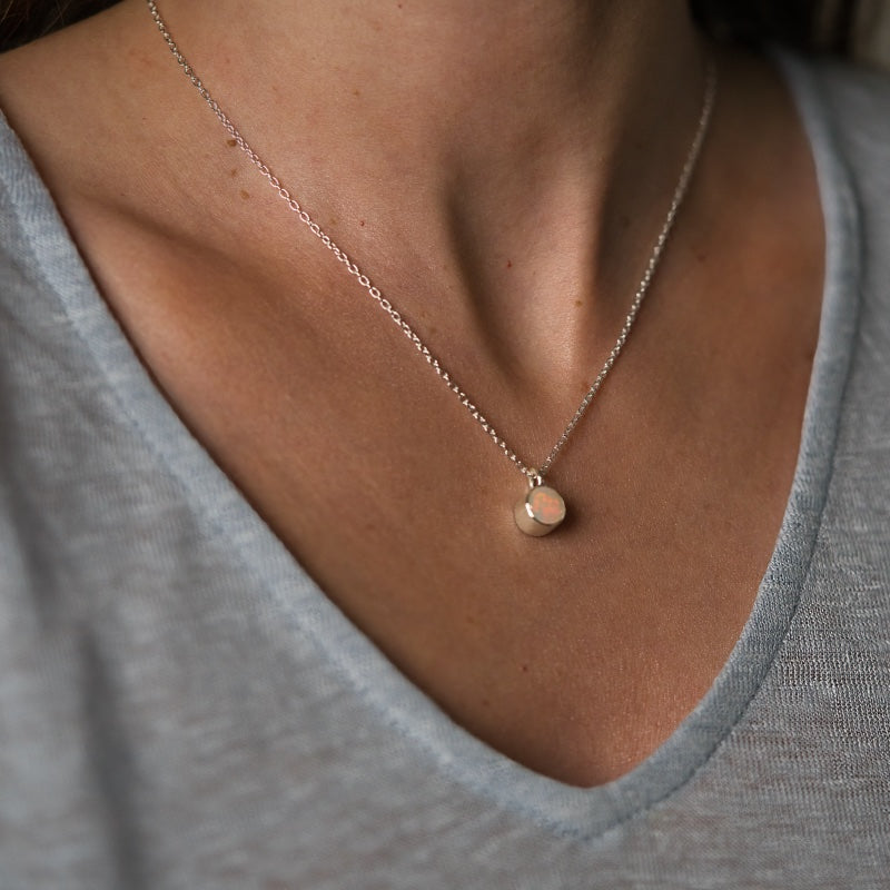 Närbild på halsband i silver med skimrande opal, buren runt en dams hals.