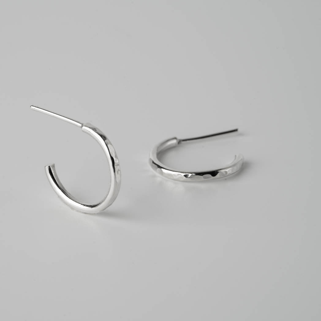 Hoops med runda hörn â handgjorda örhĂ€ngen i 925 sterlingsilver med en hamrad yta och mjuk design, fotograferade mot vit bakgrund.