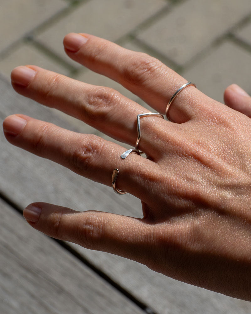 Kvinna bÀr vÄr Open silverring i Àkta silver, handen vackert placerad med marken som bakgrund.