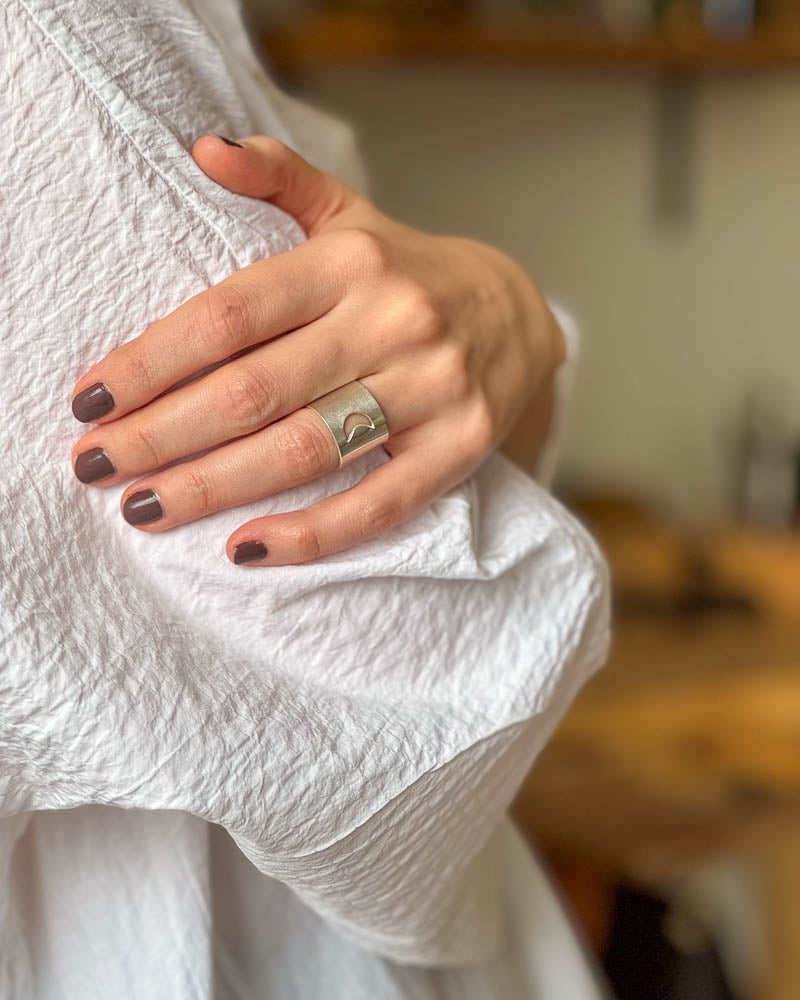 En dam som bÀr en bred silverring med en mÄnskÀra, design Nude Stockholm.