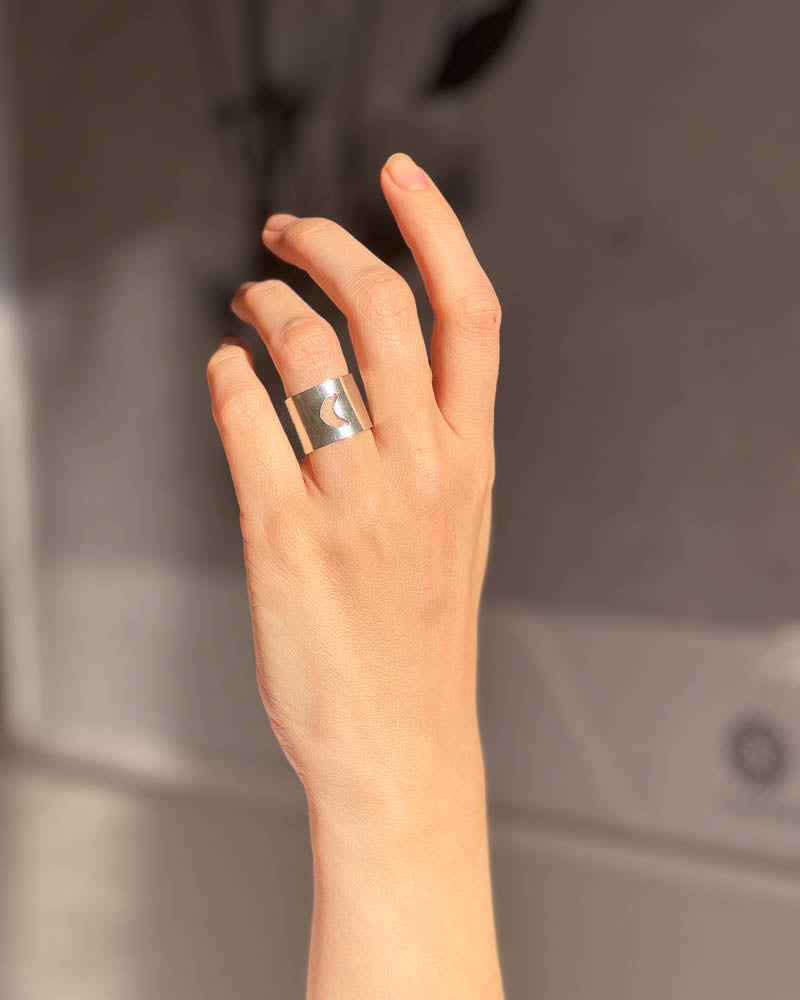 En dams hand visar en bred silverring frÄn Nude Stockholm med en utsÄgad mÄnskÀra.