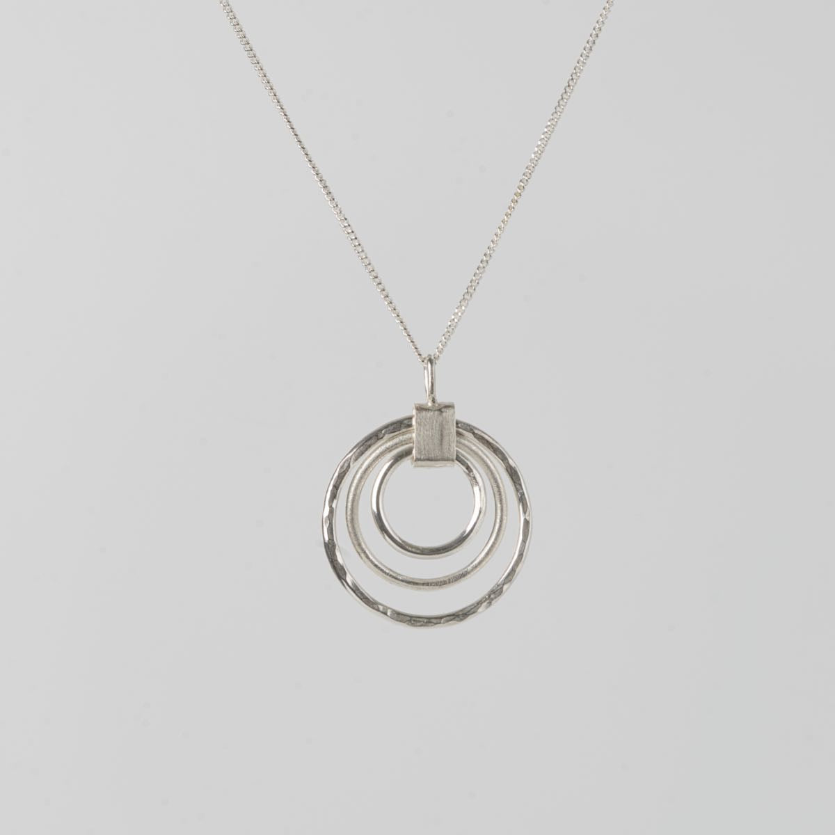 Handgjort halsband i silver från Nude Stockholm med tre cirklar i olika yta – blank, matt och hamrad – mot vit bakgrund.