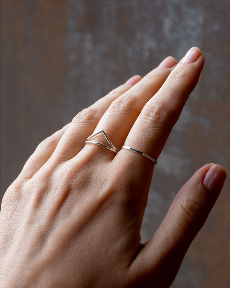 Kantig silverring i Àkta sterlingsilver buren pÄ ett pekfinger, mot en brun vÀgg.