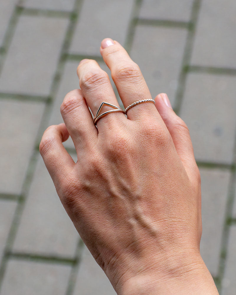 Kvinnas hand som bÀr vÄr handgjorda V-formade silverring, med en gata som bakgrund.