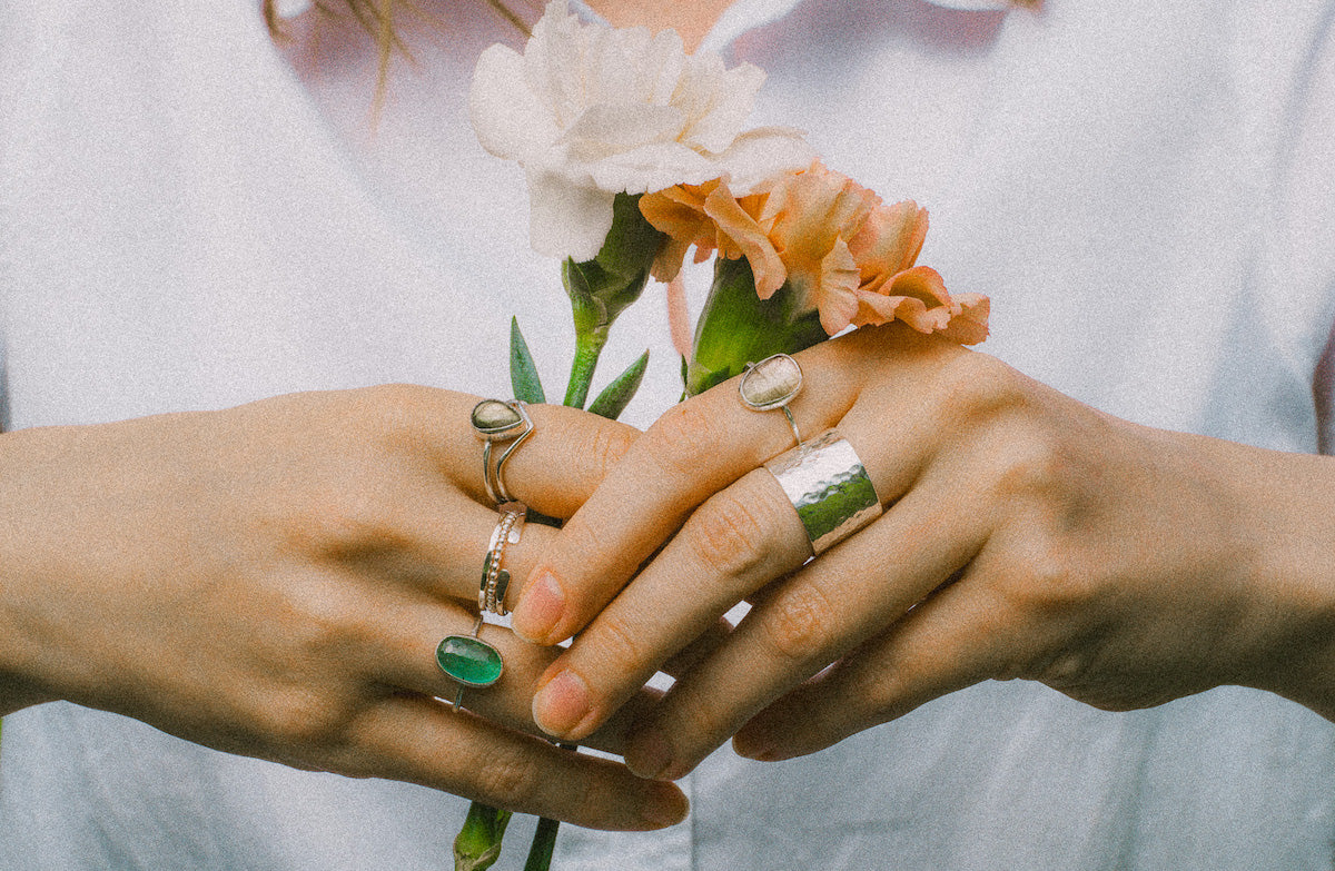 Kvinnans hand dekorerad med handtillverkade silverringar från Nude Stockholm, kompletterat med ett grepp om två blommor.