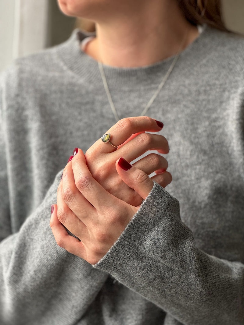 En labradorit silverring från Nude Stockholm på en kvinna som håller om sina händer.