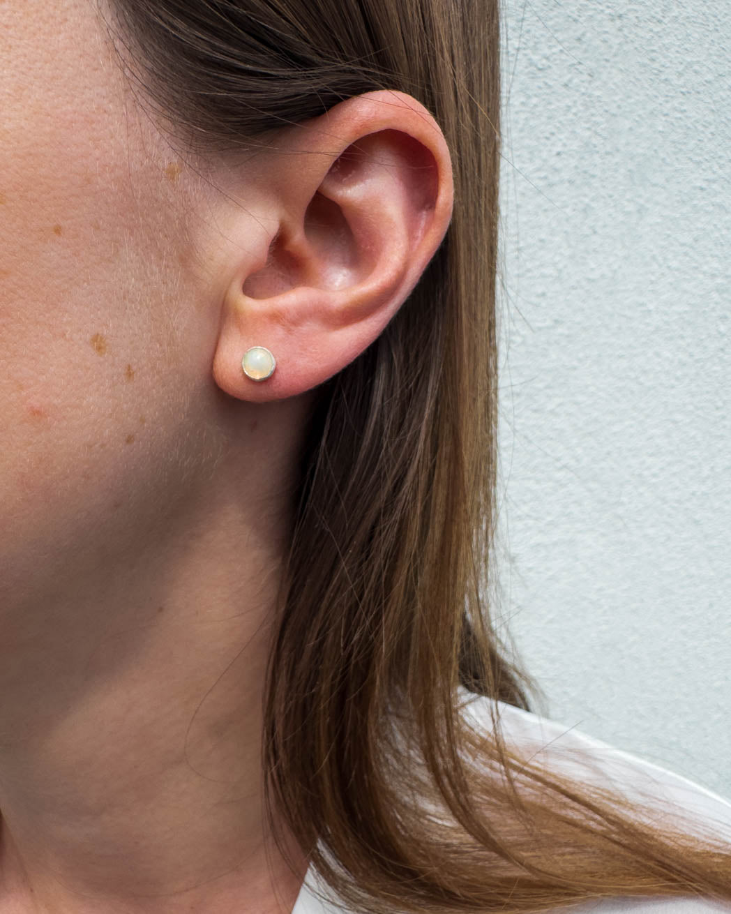 Opal studs i silver på en dams öra.