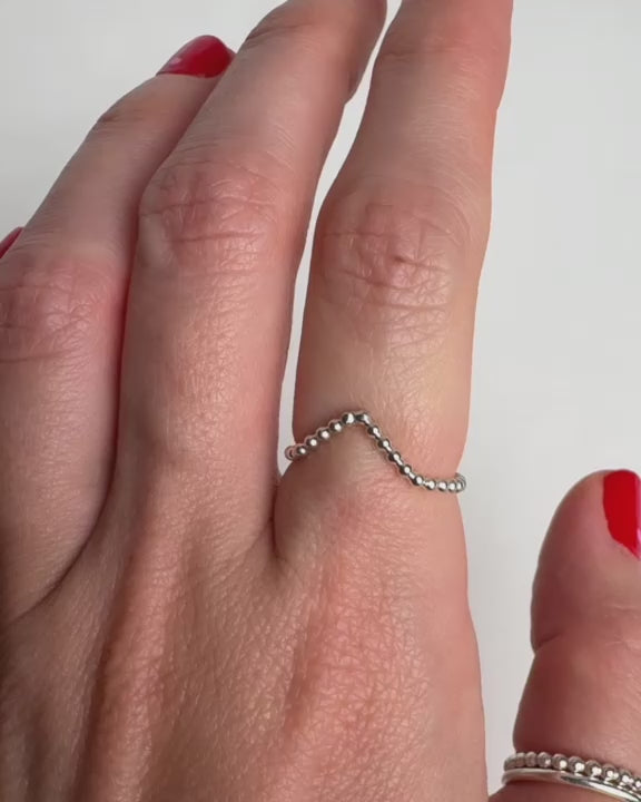 Video som visar en kvinnas hand med en V-formad silverring med små kulor, visad från olika vinklar för att framhäva ringens design.”