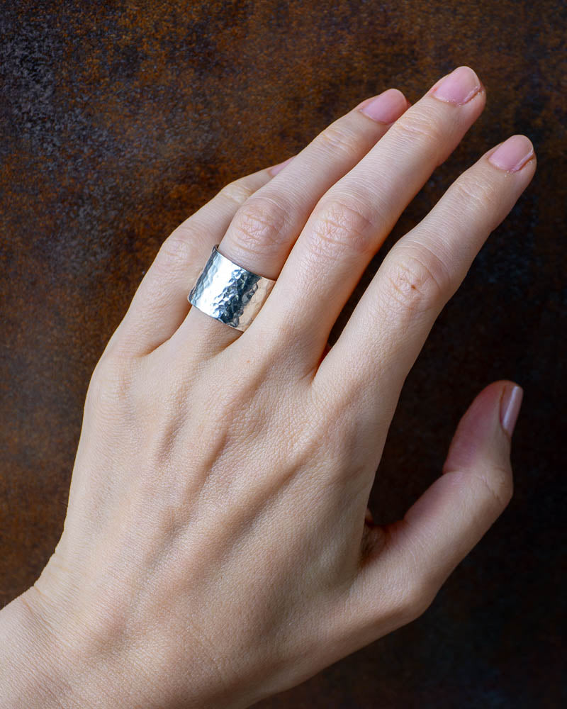 En kvinnas hand som bär på en handgjord bred silverring med hamrad textur i sterlingsilver.