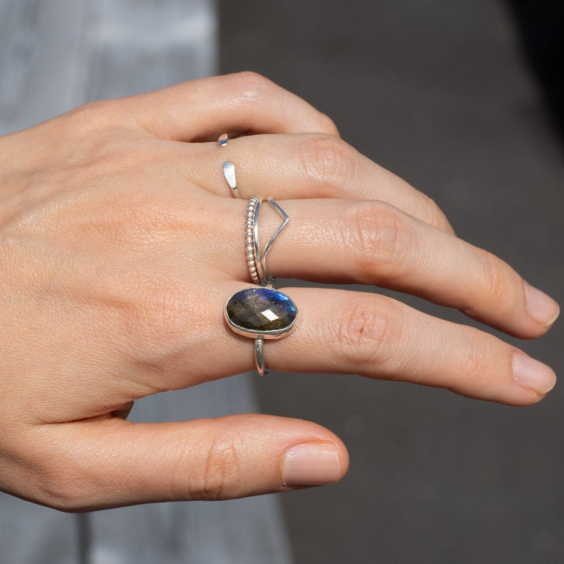 Silverring med en oval labradoritsten i äkta sterlingsilver på en hands pekfinger med marken som bakgrund.