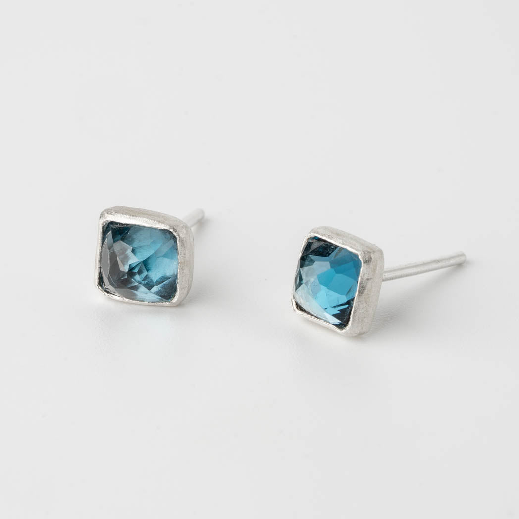 Kvadratiska studs med rosenslipade London Blue Topas-stenar, handinfattade i borstat silver, fotograferade mot vit bakgrund.